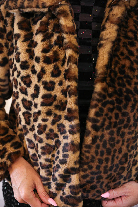 Close-up of a leopard print coat with a person's hand holding it.