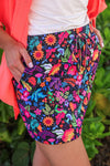 Person wearing colorful floral shorts with a green leafy background