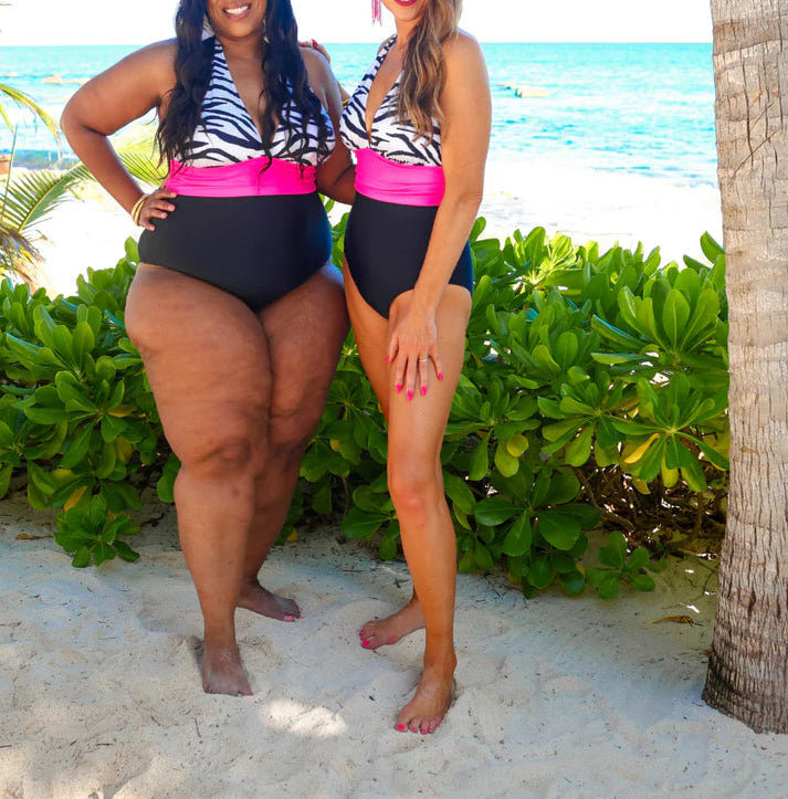 Two women in matching zebra print and pink swimsuits standing on a beach.
