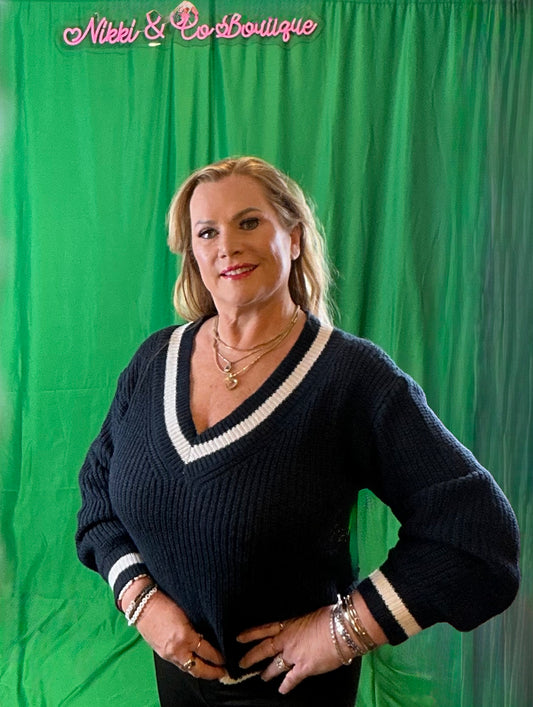 Woman wearing a black sweater with white trim against a green backdrop with 'Nikki & Co Boutique' text.