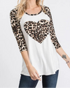 Woman wearing a white top with a leopard print heart design and matching sleeves on a plain background