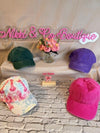 Colorful baseball caps on a stone surface with 'Nikki & Co Boutique' sign in the background.