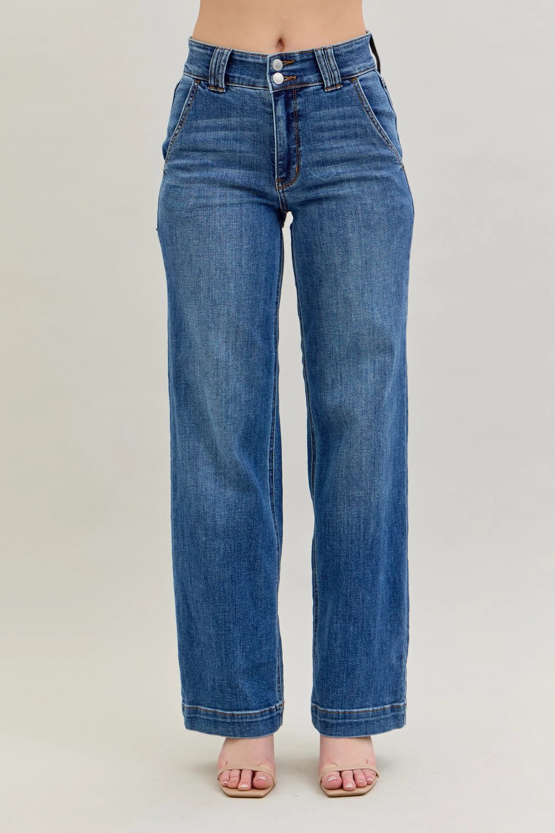 A person wearing medium-wash blue denim jeans with a straight-to-wide leg fit, shown from the waist down against a plain light gray studio background.