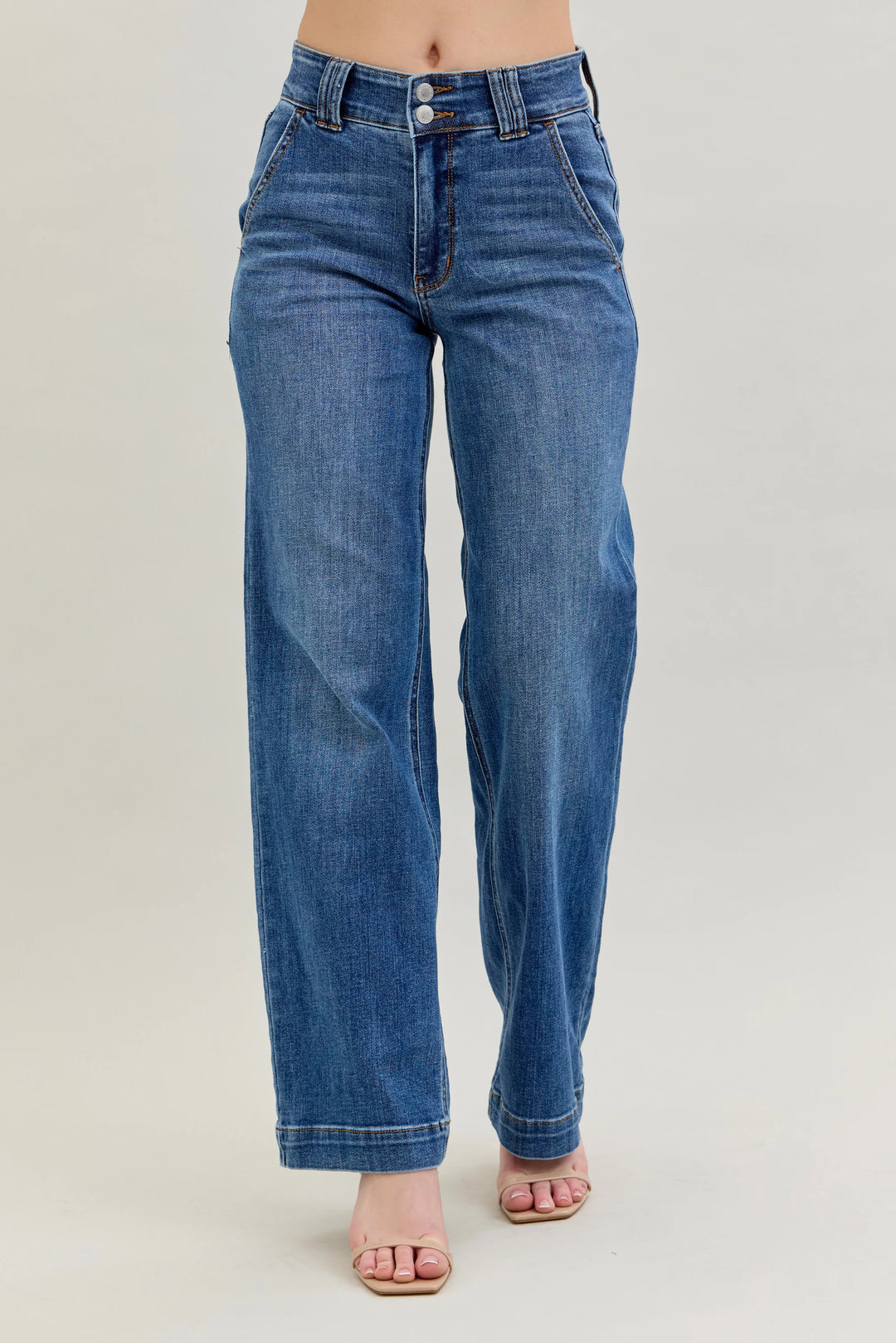 A person wearing medium-wash blue denim jeans with a straight-to-wide leg fit, shown from the waist down against a plain light gray studio background.