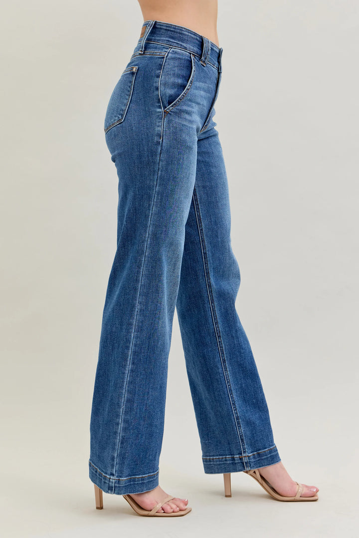 A person wearing medium-wash blue wide-leg jeans with rolled cuffs and nude high-heel sandals, shown from the waist down against a plain light beige studio background.