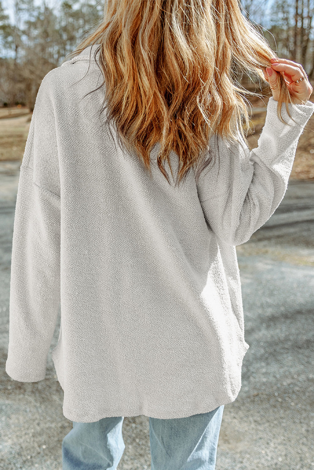 Person wearing a beige cardigan and light blue jeans standing on a road with trees in the background