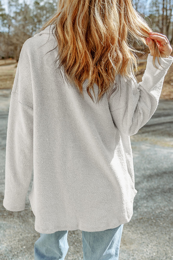 Person wearing a beige cardigan and light blue jeans standing on a road with trees in the background
