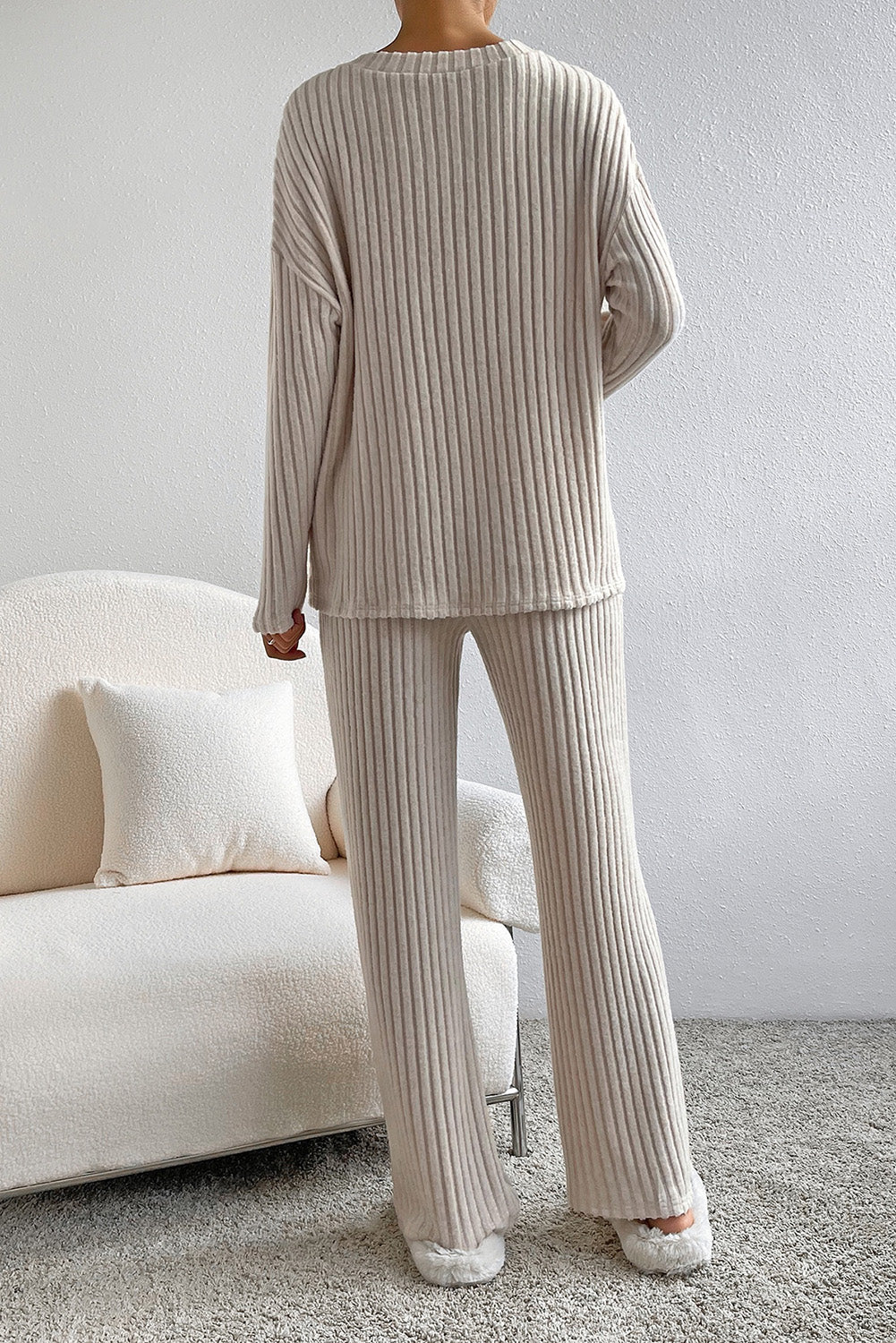 Person wearing a beige ribbed sweater and pants in a minimalistic room.