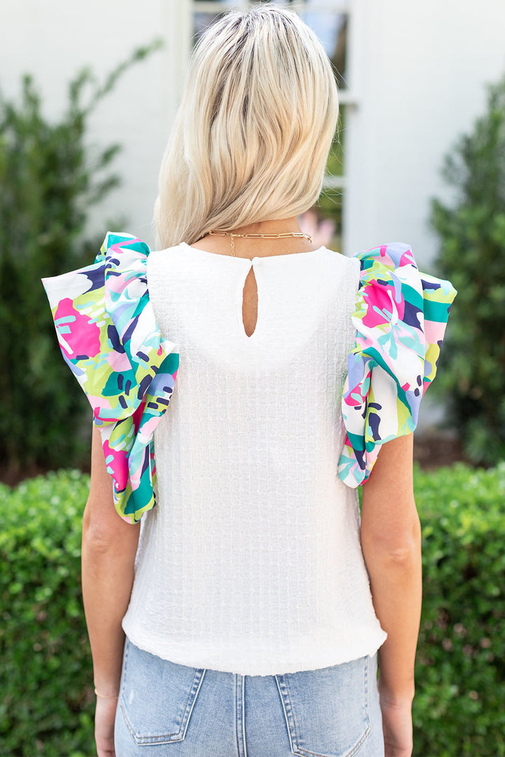 Woman wearing a white top with colorful floral ruffled sleeves outdoors.