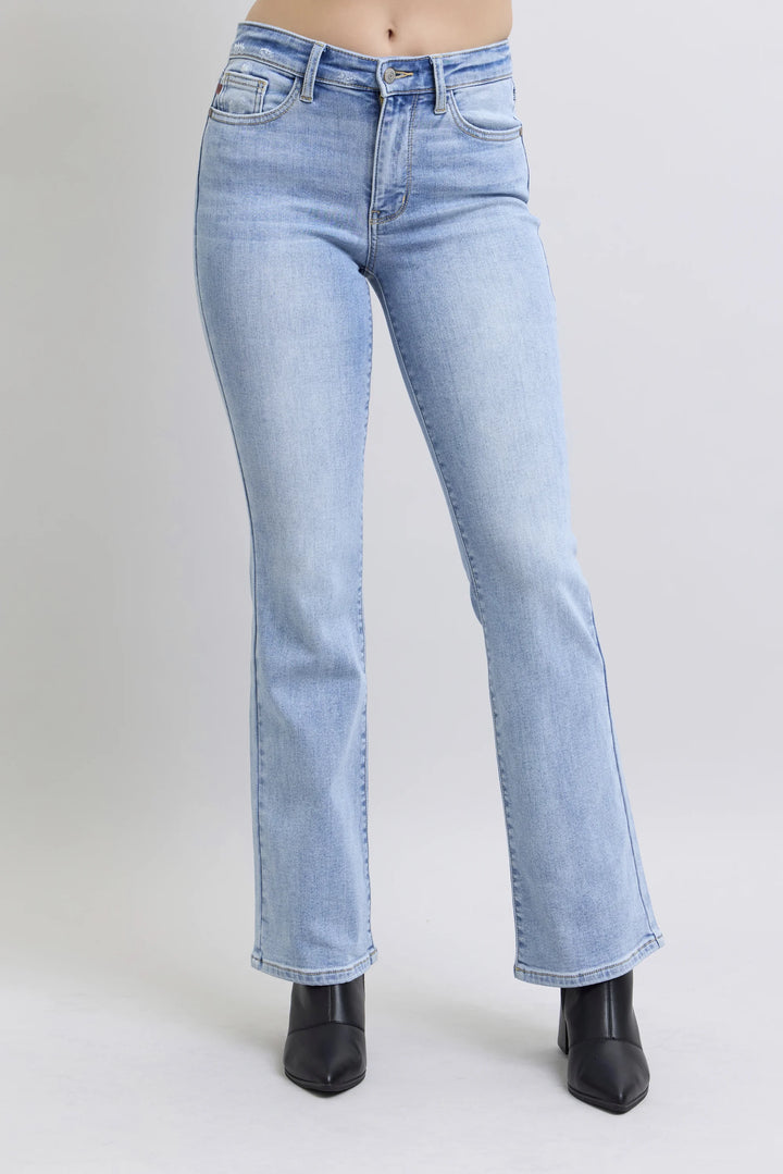 A person wearing light-wash blue denim jeans with a straight-to-flare leg and black pointed-toe boots, shown from the waist down against a light gray studio background.