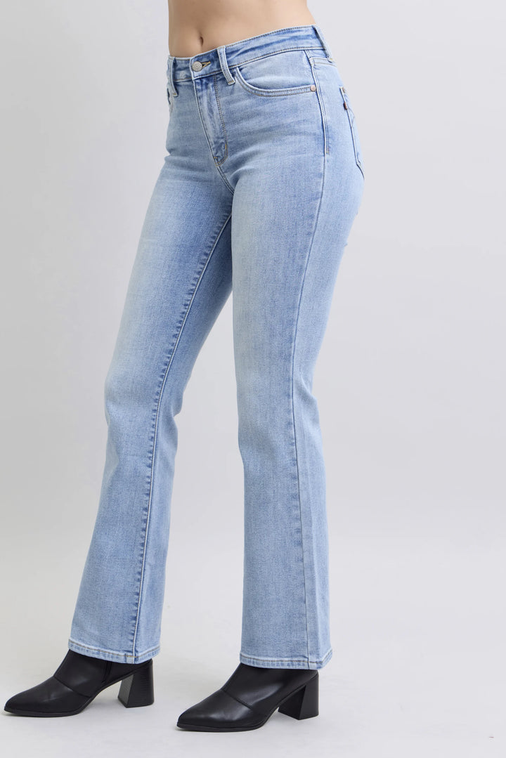 Light wash blue denim jeans shown on a model from the waist down, paired with black pointed-toe heeled boots against a light gray studio background.