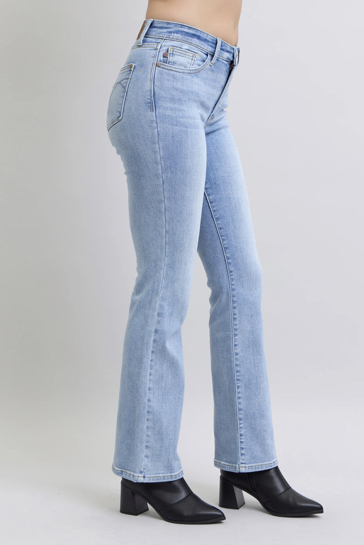 Light wash blue denim jeans shown on a model from the side, paired with black pointed-toe heeled boots against a plain light gray studio background.