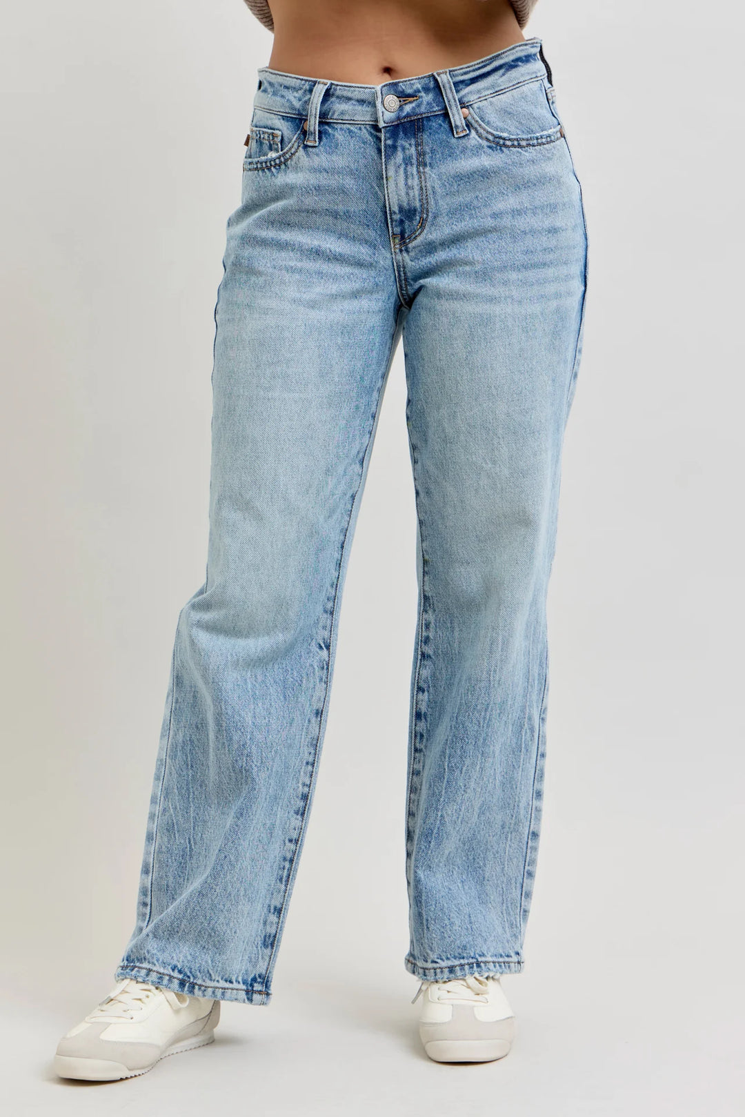 A person wearing light-wash blue straight-leg jeans and white sneakers, shown from the waist down against a plain light gray studio background.