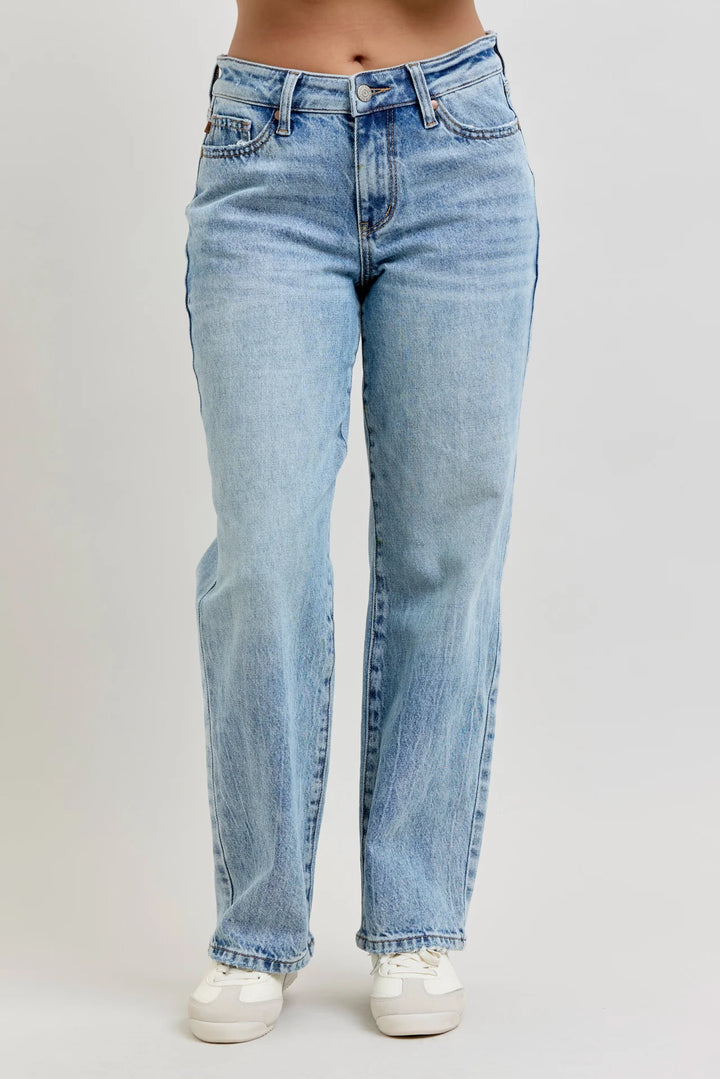 A person wearing light-wash blue denim jeans and white sneakers, shown from the waist down against a plain light gray studio background.