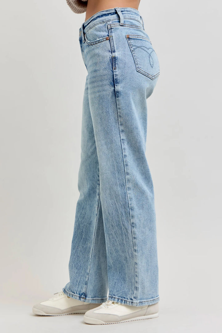 A person wearing light-wash blue wide-leg jeans and white sneakers, shown from the waist down against a plain light gray studio background.