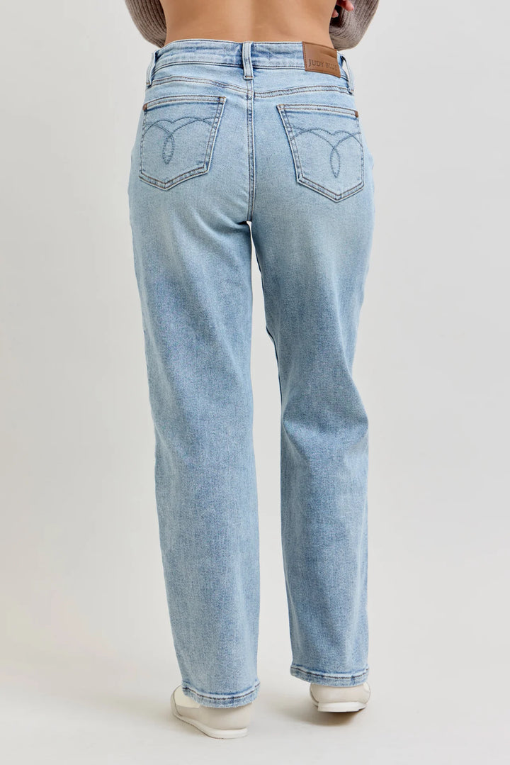 A person shown from the back wearing light-wash blue jeans with a brown leather patch on the back waistband, photographed against a plain light gray studio background.