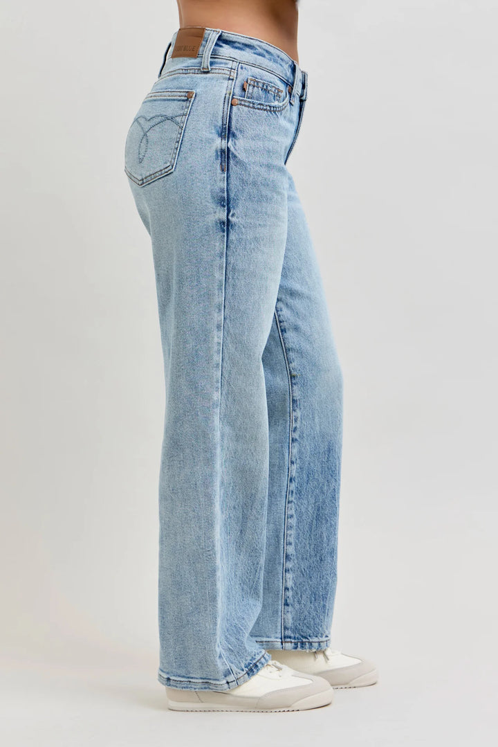 A side profile view of a person wearing light-wash blue wide-leg jeans and white sneakers against a plain light gray studio background.