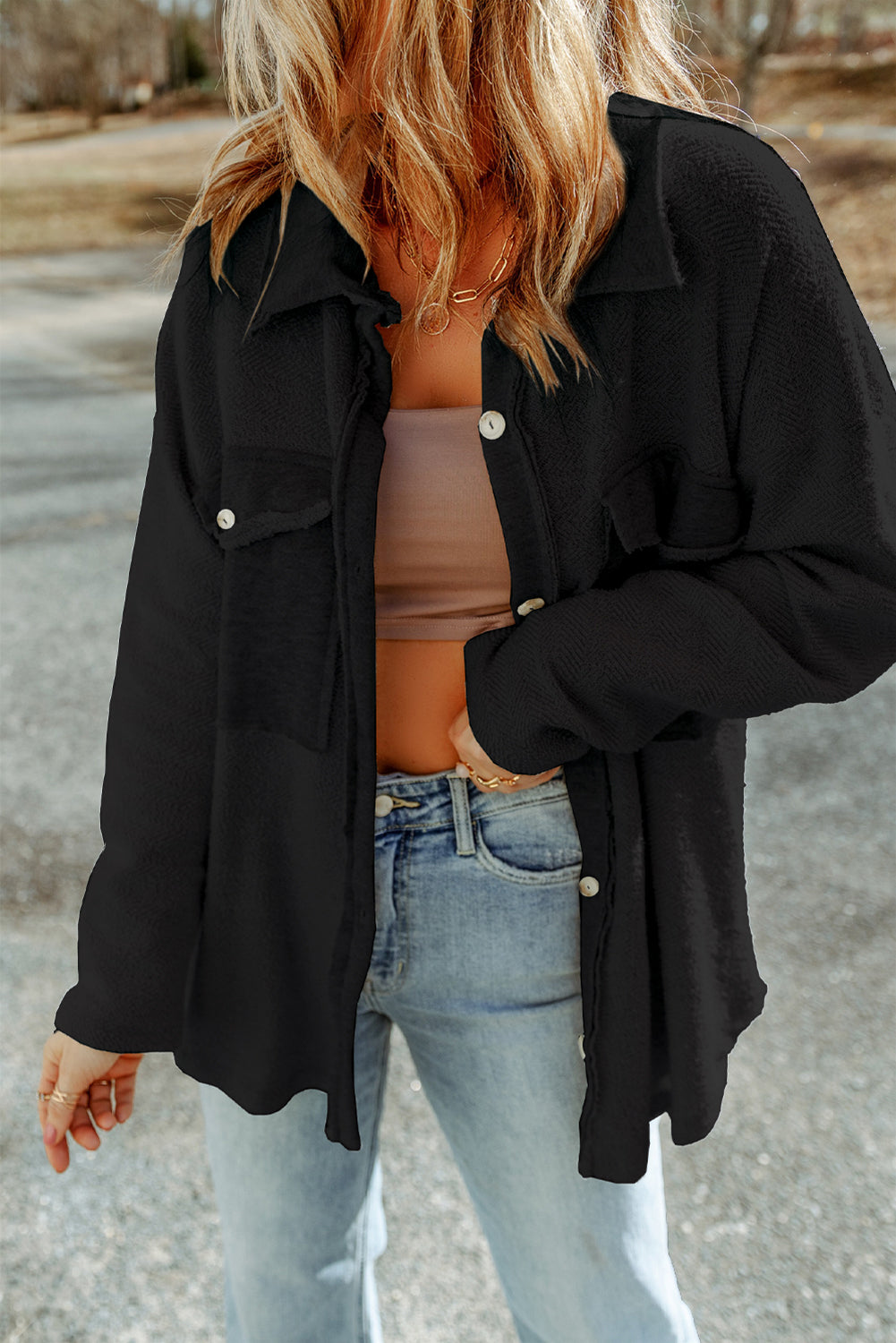 Person wearing a black jacket over a brown top and light blue jeans on a road background