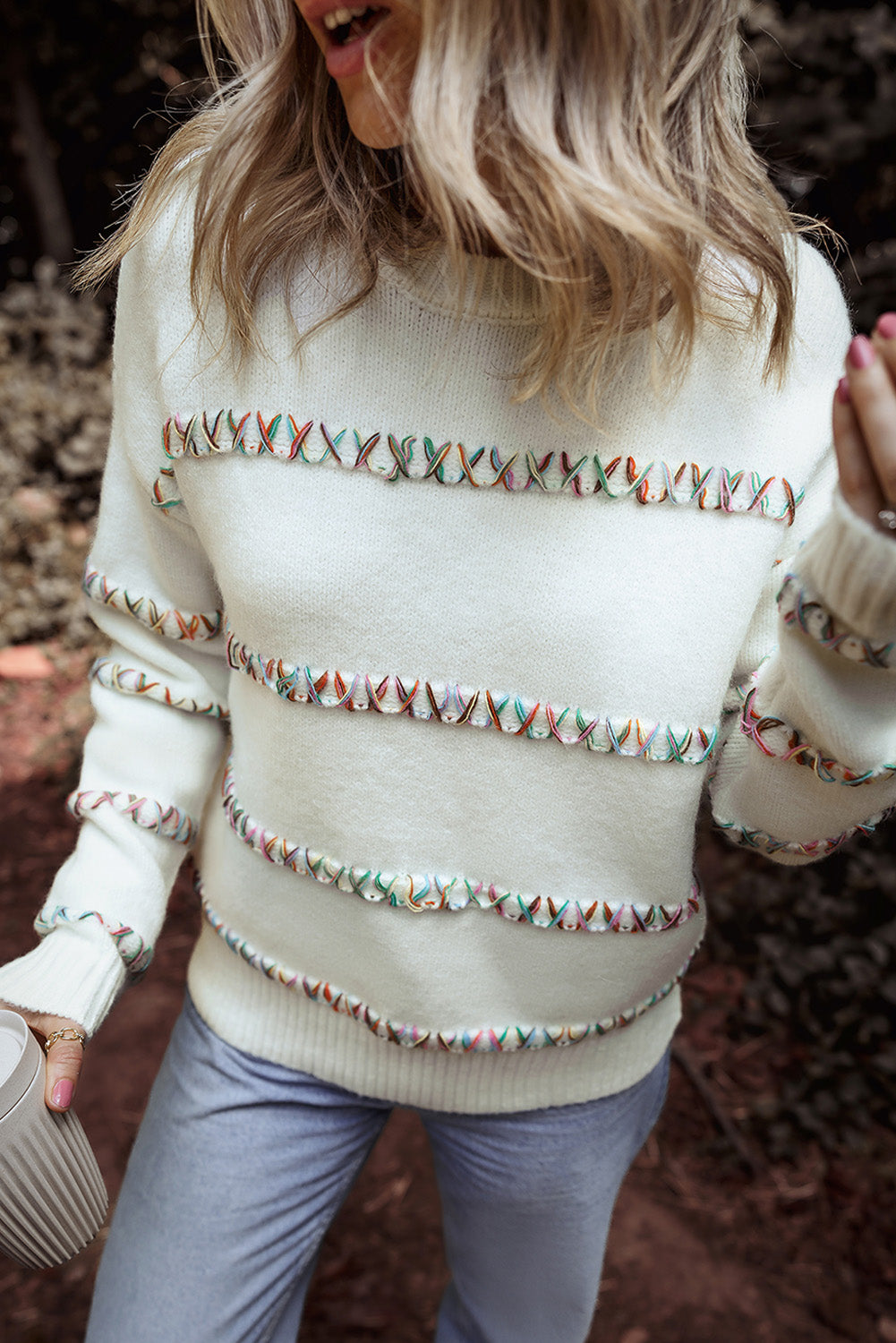 Person wearing a white sweater with decorative patterns in an outdoor setting