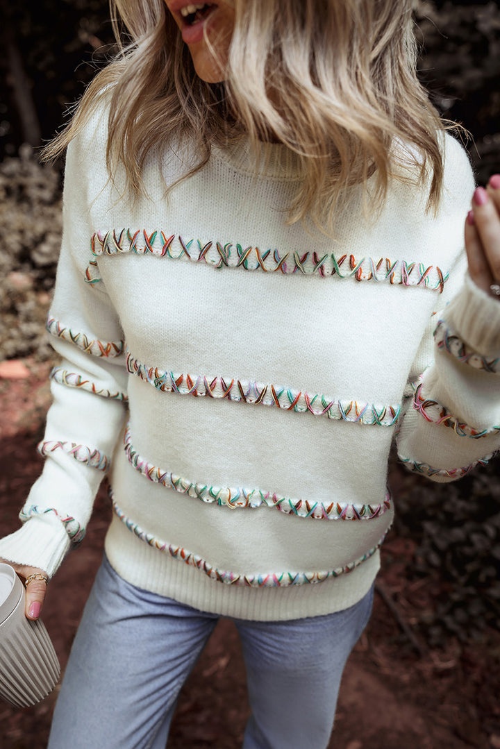 Person wearing a white sweater with decorative patterns in an outdoor setting
