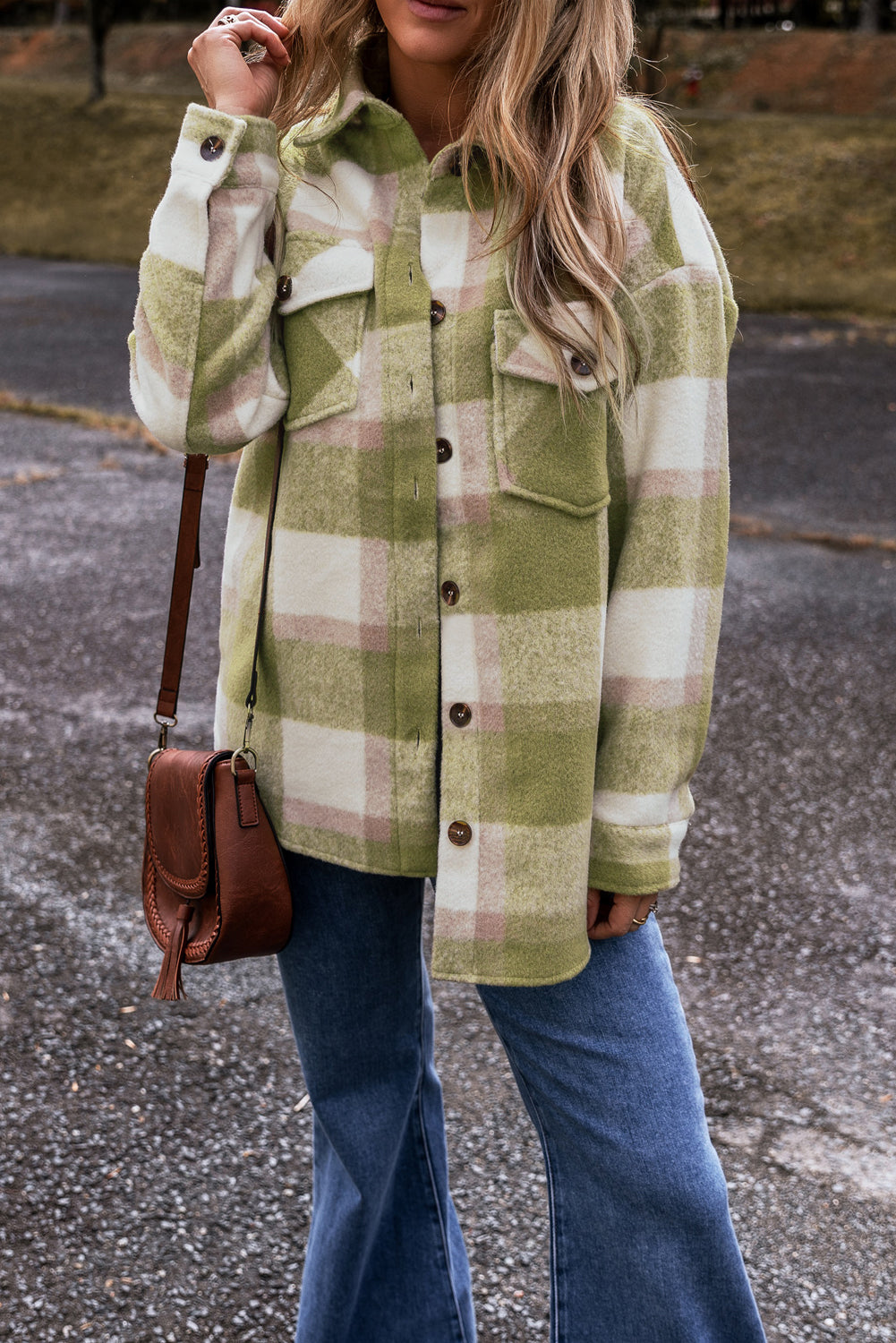 Person wearing a green plaid shirt with a brown leather bag on a street.