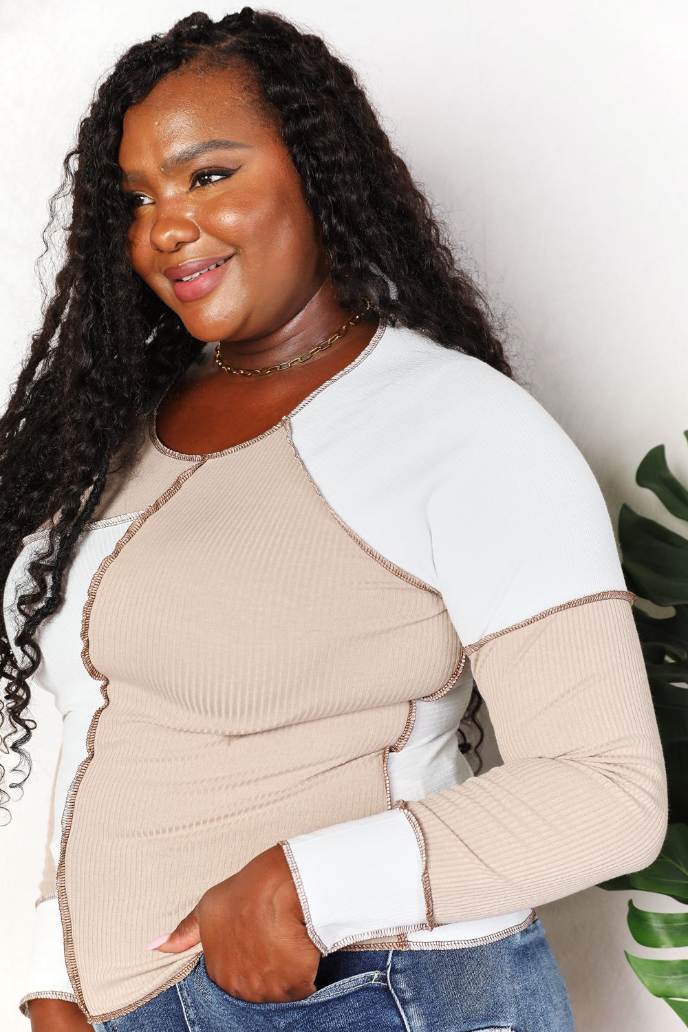 Woman wearing a beige and white long-sleeve top with a plant in the background