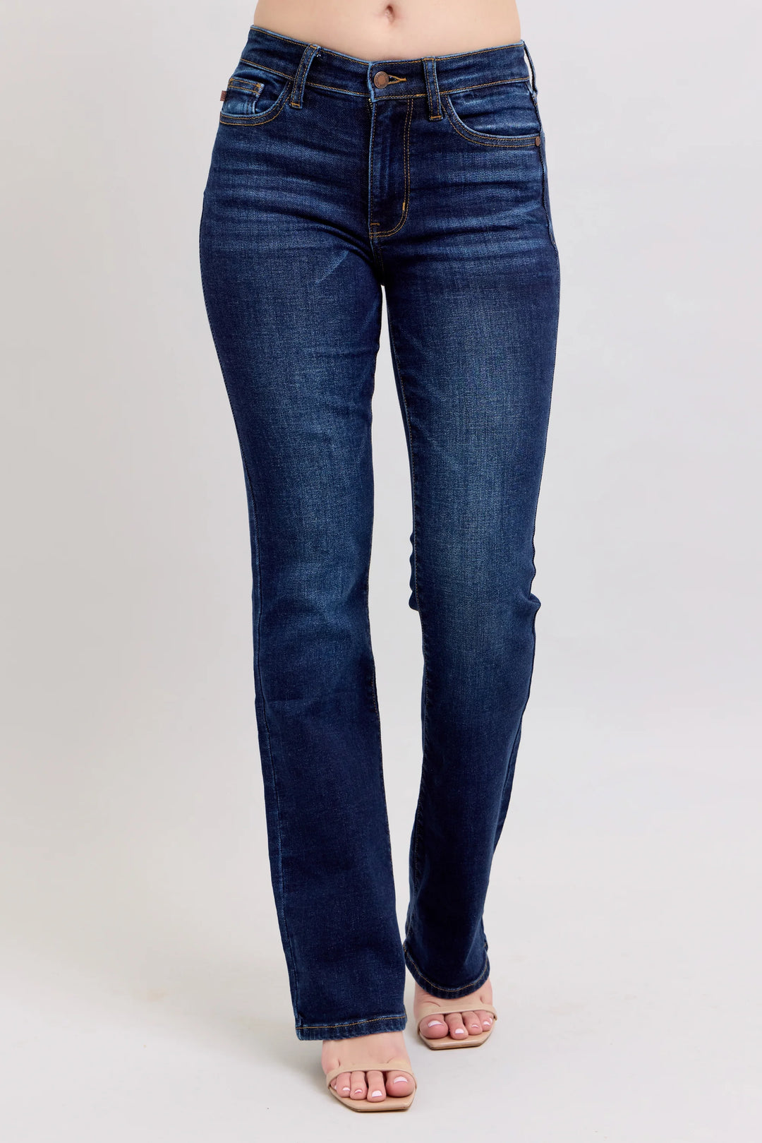 A person wearing dark blue straight-leg denim jeans and light pink sandals, shown from the waist down against a light gray studio background.