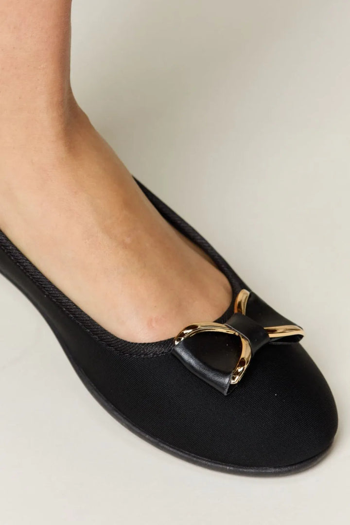 Black flat shoe with a gold buckle on a light background