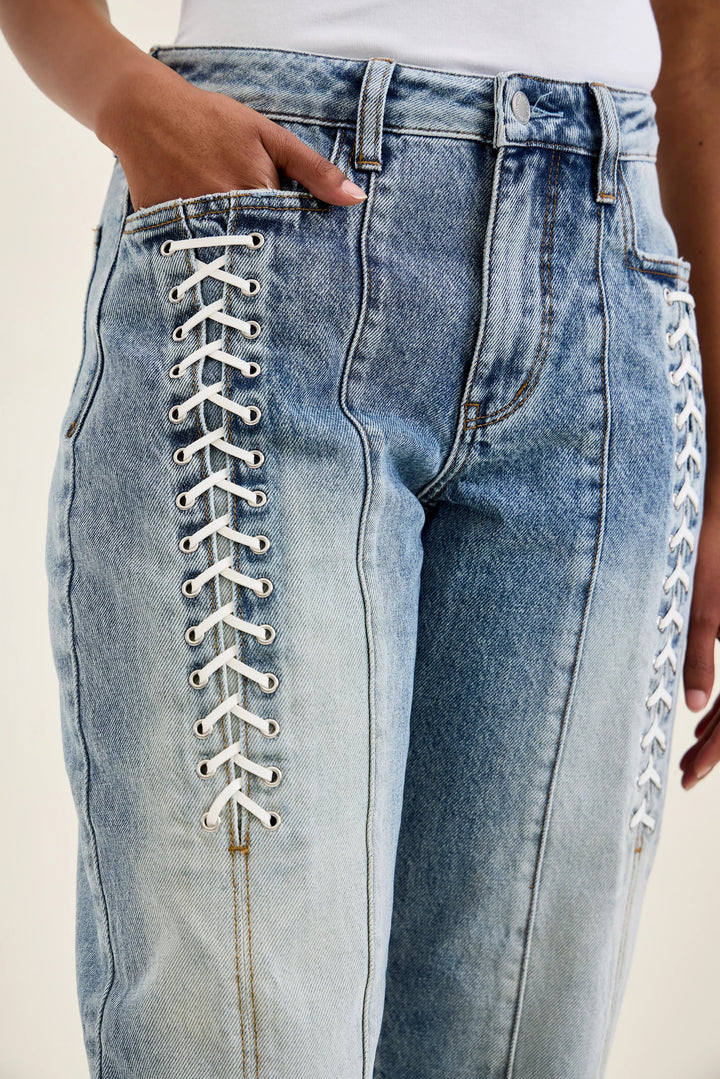 Close-up of a person wearing light blue denim jeans with decorative white lace-up detailing running down the front of each leg.