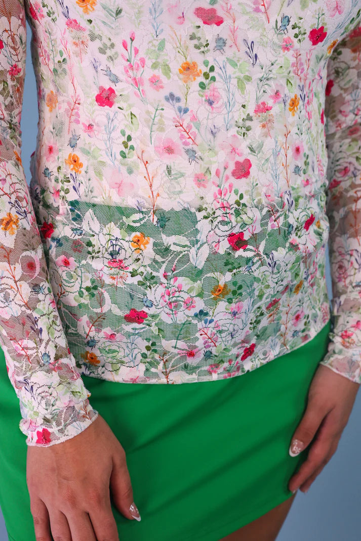 Person wearing a floral blouse with long sleeves and a green skirt against a blue background