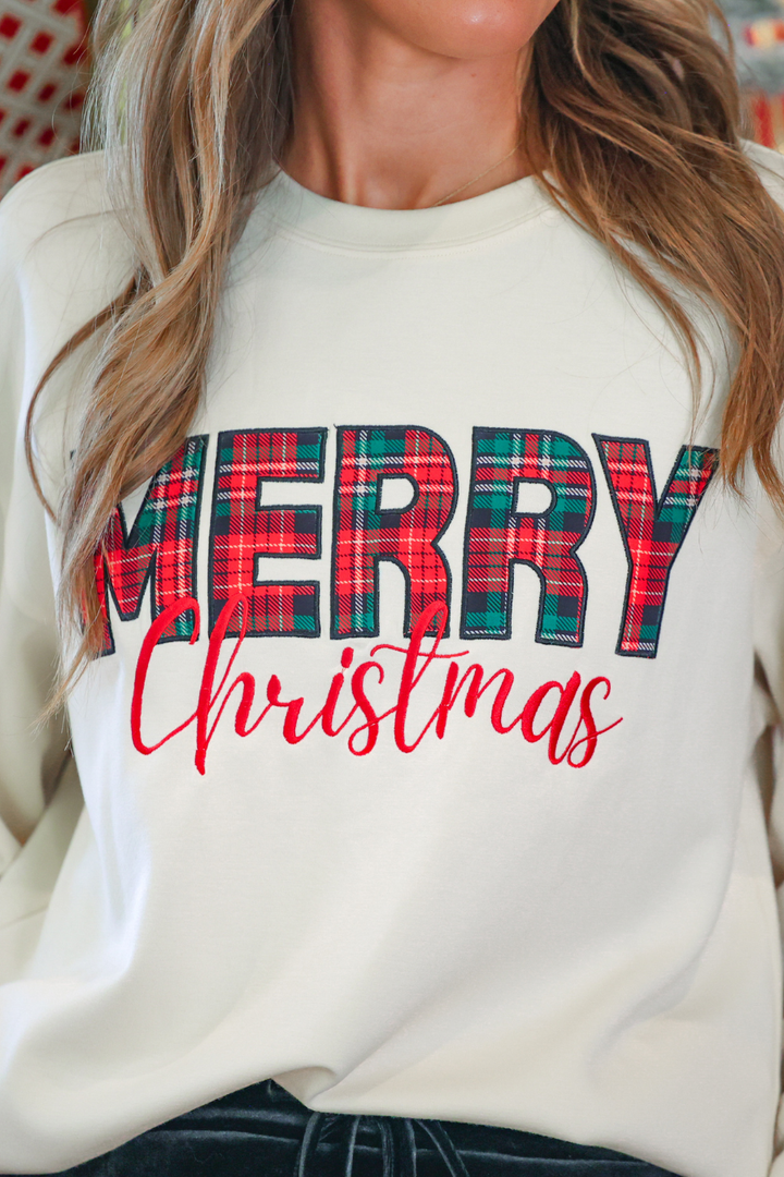 A close-up of a woman wearing a cream-colored crewneck sweatshirt with a &