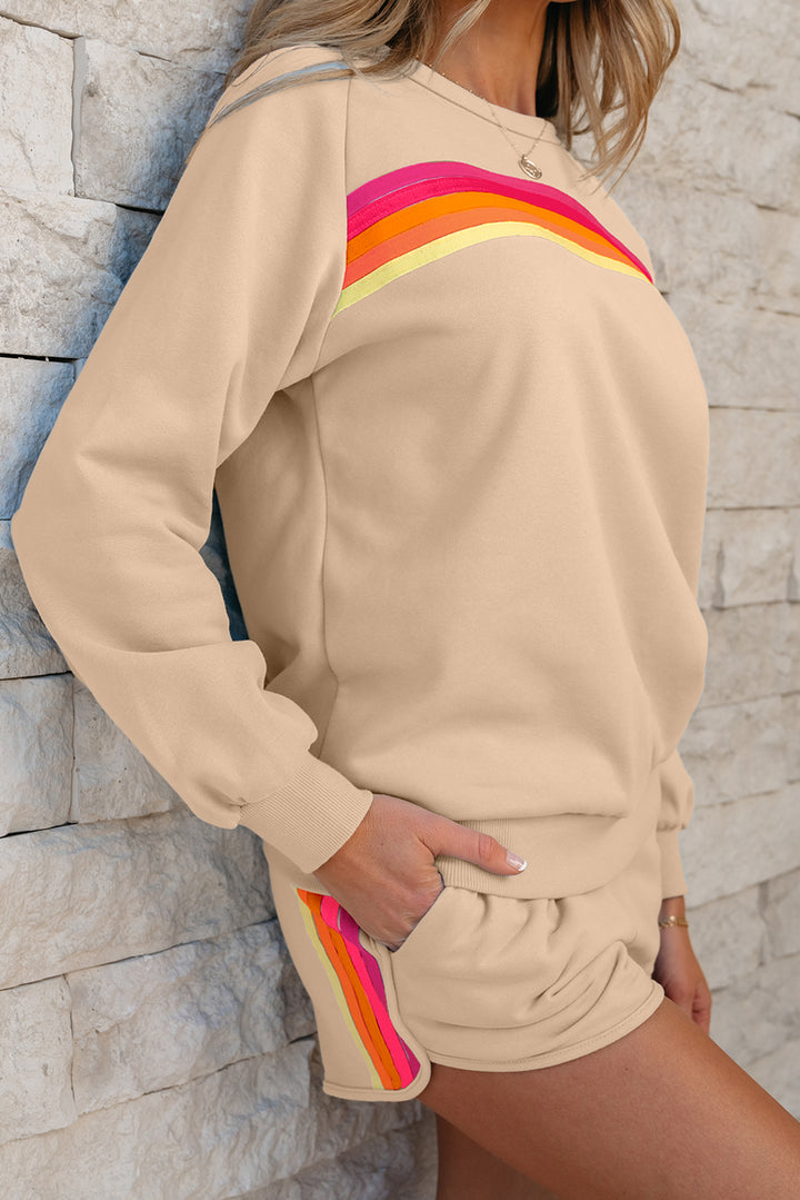 Person wearing a beige outfit with colorful stripes against a stone wall.