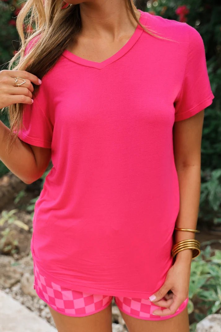 Woman wearing a hot pink, v neck tee and pink checkered shorts.