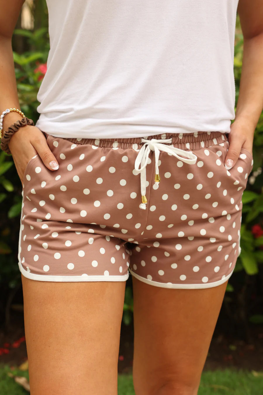 Person wearing brown polka dot shorts with a white top against a blurred green background