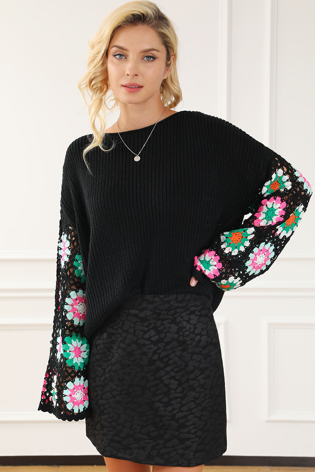 Woman wearing a black sweater with colorful floral sleeves and a matching skirt against a white wall.