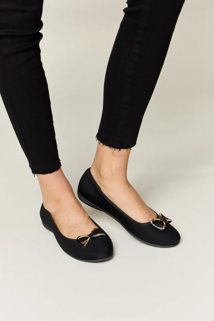 Black flats worn with black pants on a light background