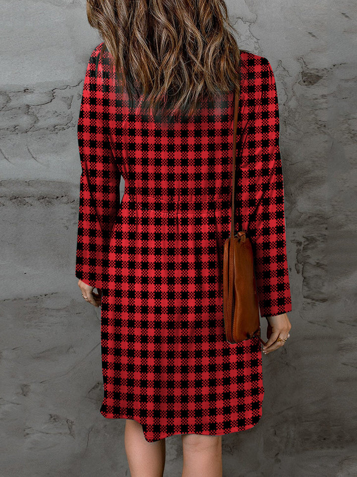 Person wearing a red and black plaid dress against a gray wall.