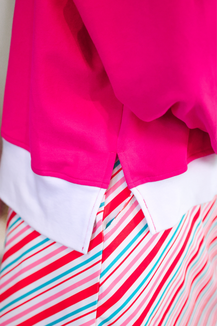 Close-up of a bright pink garment with a white hem, layered over a red, pink, and blue striped fabric.