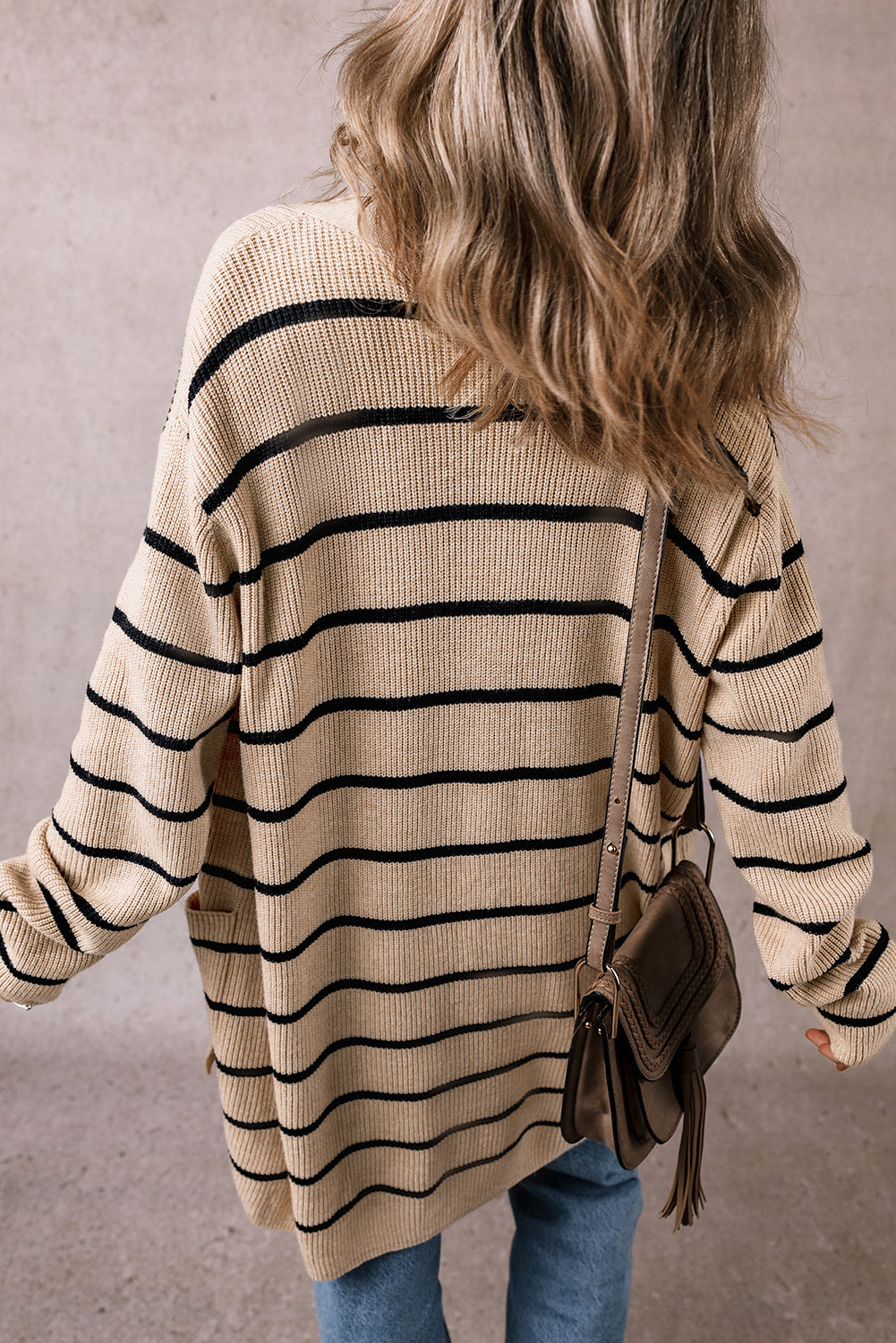 Person wearing a beige and black striped sweater with a brown leather bag on a neutral background