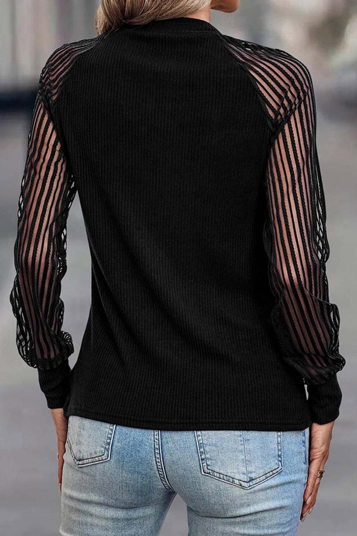 Black sweater with sheer sleeves worn by a person, standing on a blurred background