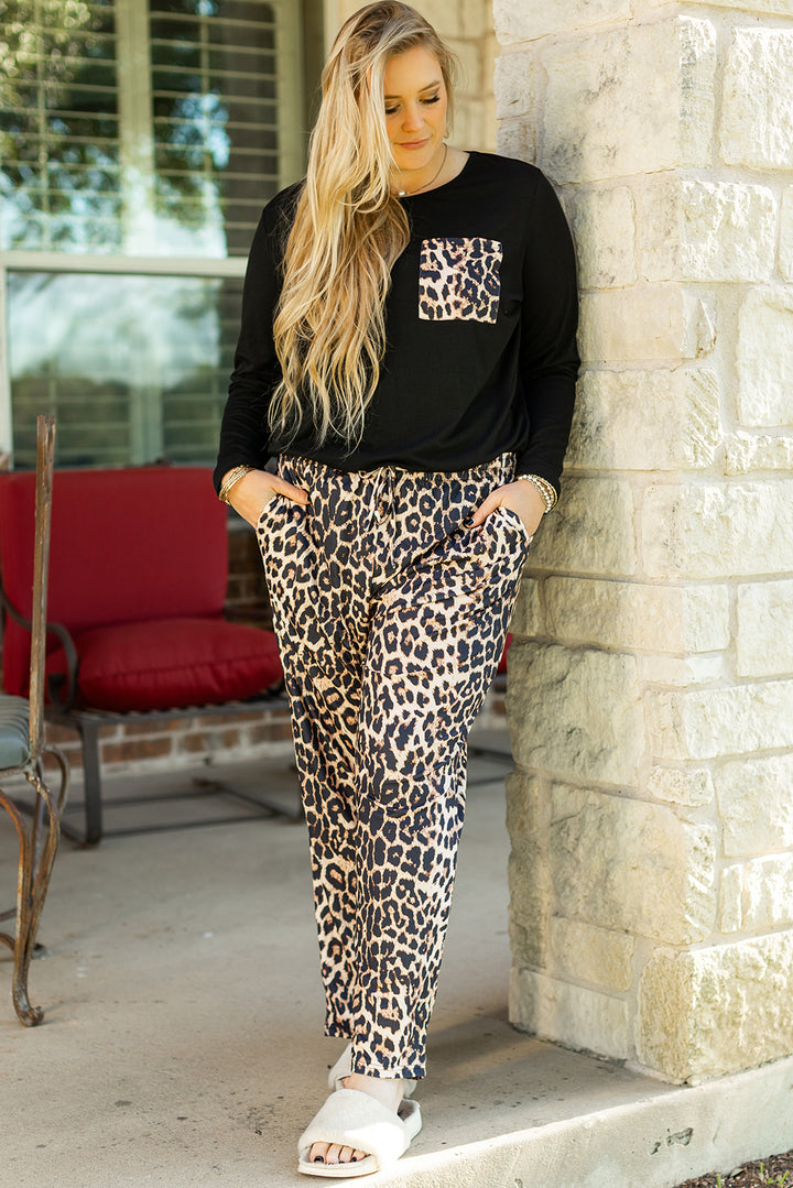 Woman wearing a black sweatshirt with a leopard print design and leopard print pants, standing against a stone wall.