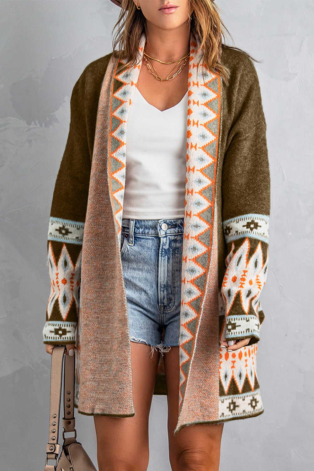 Person wearing a long, patterned cardigan over a white top and denim shorts on a gray background