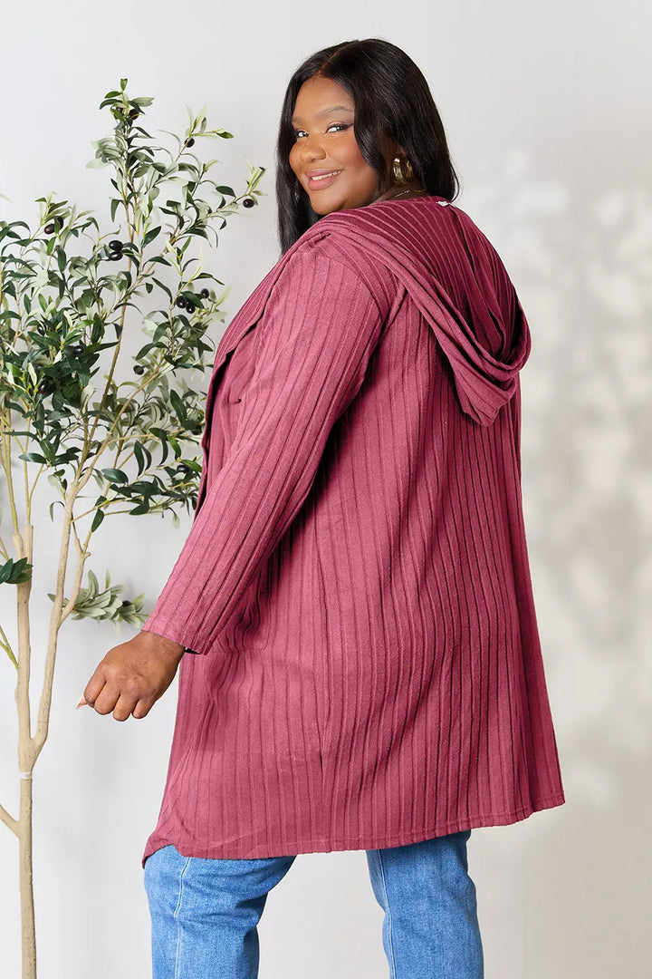 Woman wearing a ribbed pink sweater with a hood against a white background