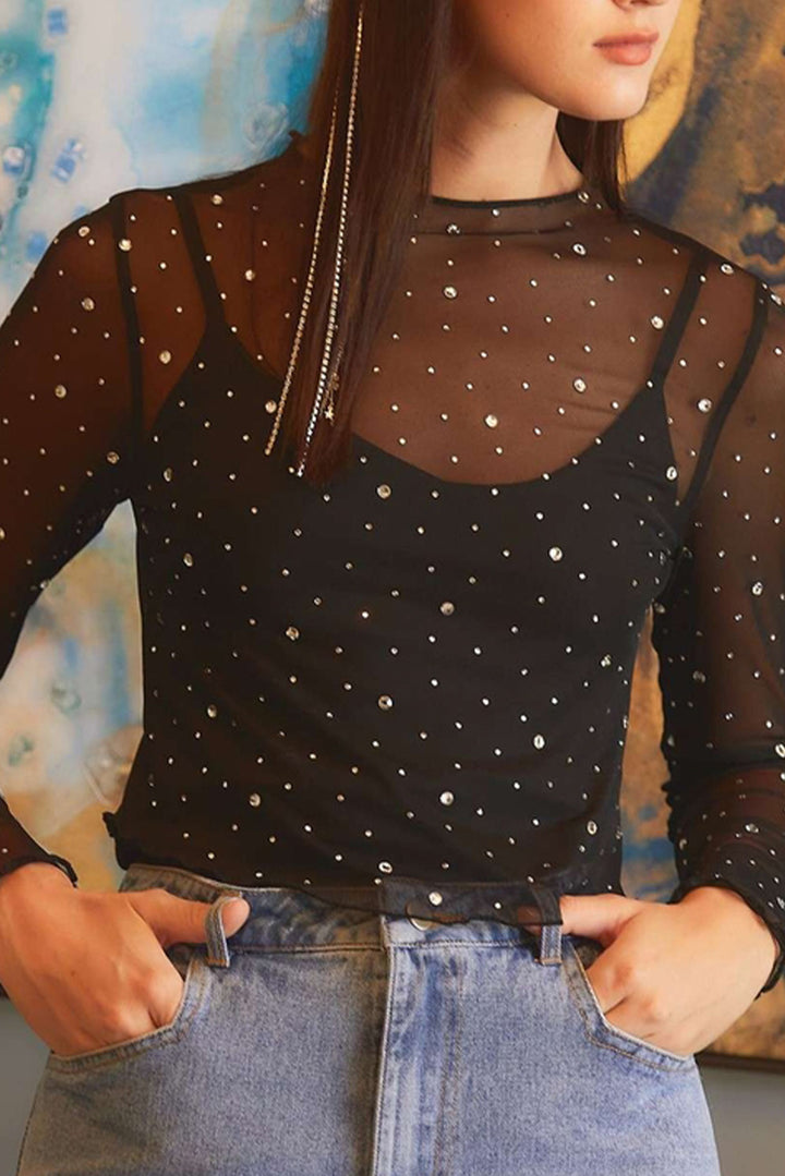 Person wearing a black long-sleeve top with gem design and blue jeans against a colorful abstract background.