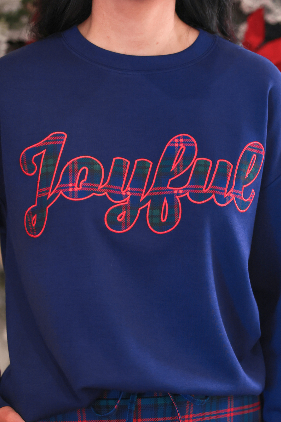 A close-up of a person wearing a royal blue crewneck sweatshirt with the word &