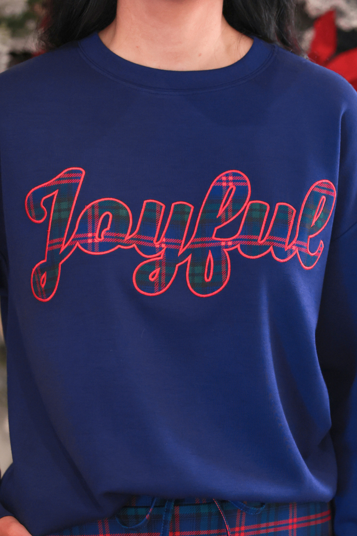A close-up of a person wearing a royal blue crewneck sweatshirt with the word &