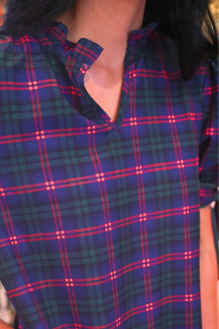 Close-up of a plaid short-sleeve top worn by a model, featuring a navy blue base with green and red intersecting plaid lines.