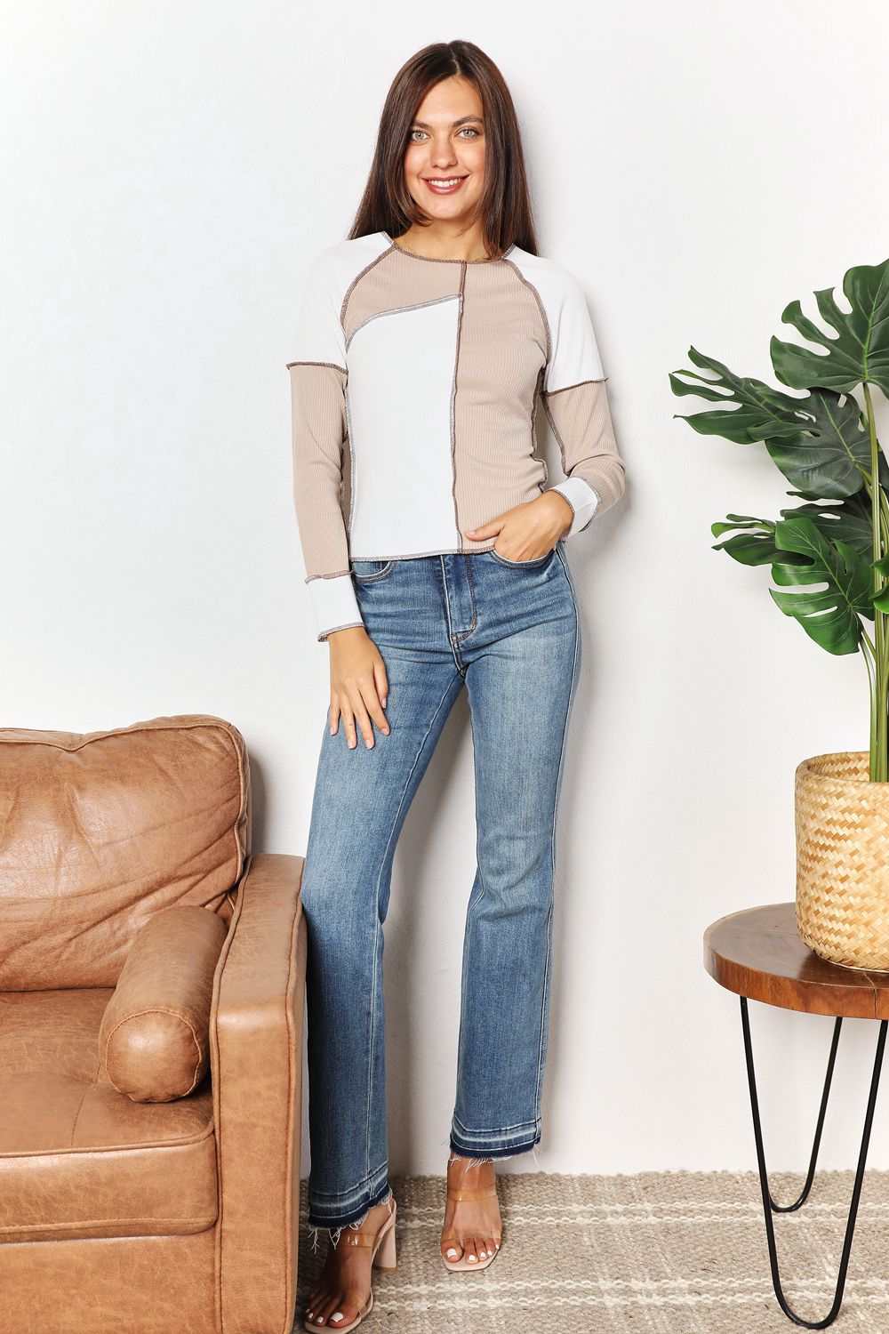 Woman standing in a living room with a brown leather couch and a plant.