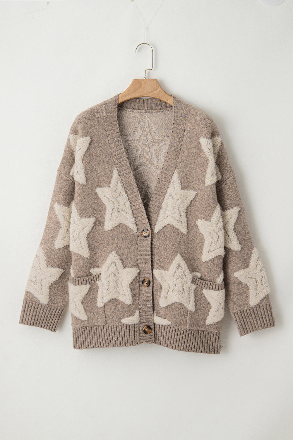 Brown cardigan with star patterns on a wooden hanger against a white background