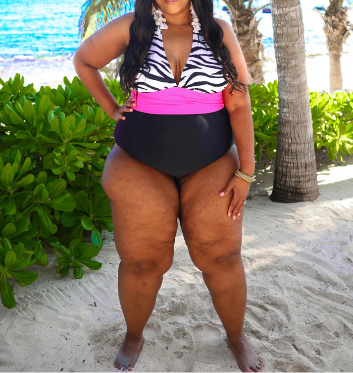 Woman in a zebra print and pink swimsuit on a beach with palm trees and ocean in the background.